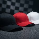Três bonés lisos sobre asfalto com bandeira quadriculada ao fundo — bonés personalizados para automobilismo