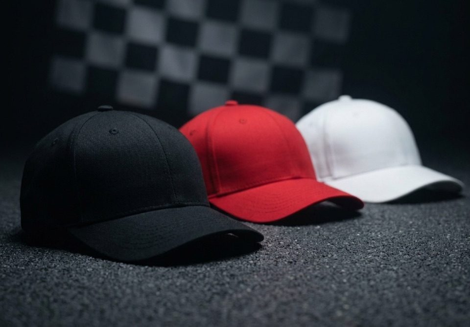 Três bonés lisos sobre asfalto com bandeira quadriculada ao fundo — bonés personalizados para automobilismo